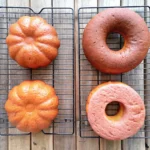 Close-up of a pumpkin-shaped bread and a bagel-like pastry on a wire cooling rack, set on a rustic wooden surface.