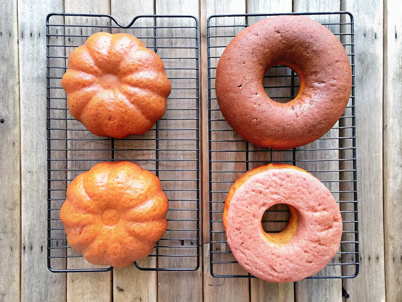 Close-up of a pumpkin-shaped bread and a bagel-like pastry on a wire cooling rack, set on a rustic wooden surface.